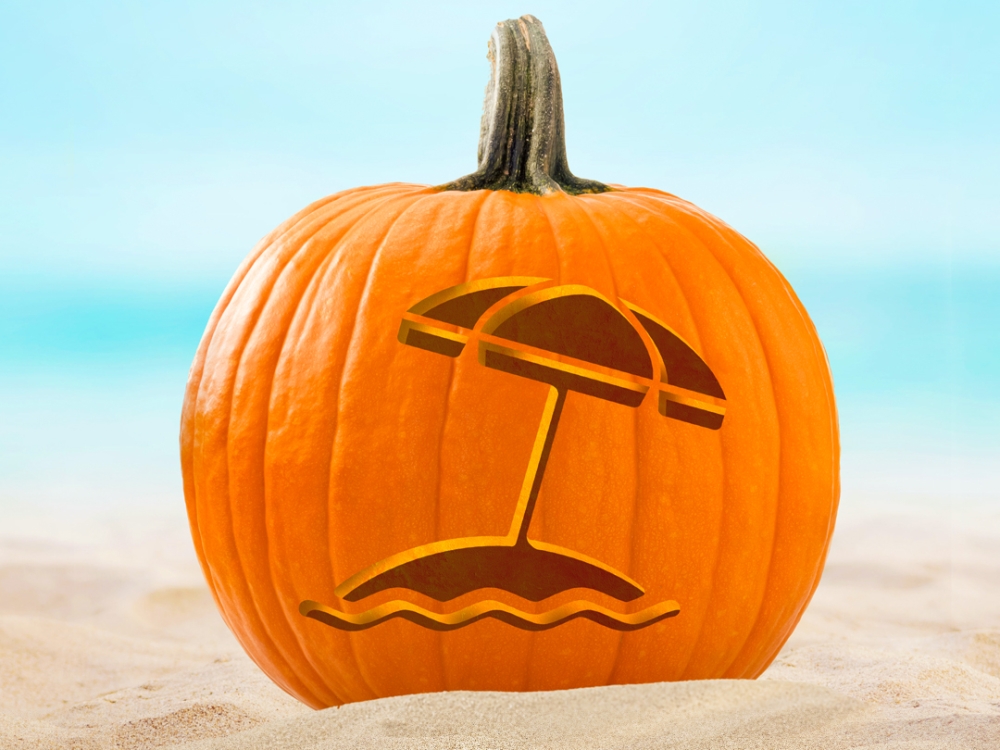 A pumpkin on a beach with an umbrealla carved into it.