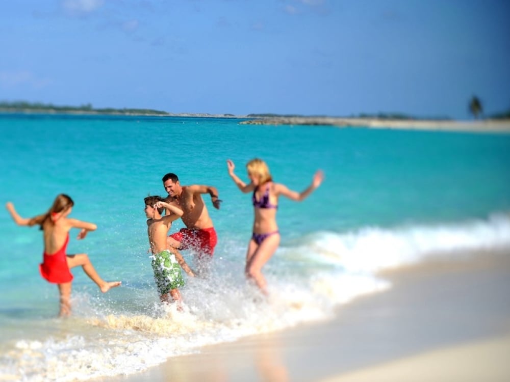 A family of four splashes in the turquoise waters of Nassau Paradise Island, Bahamas