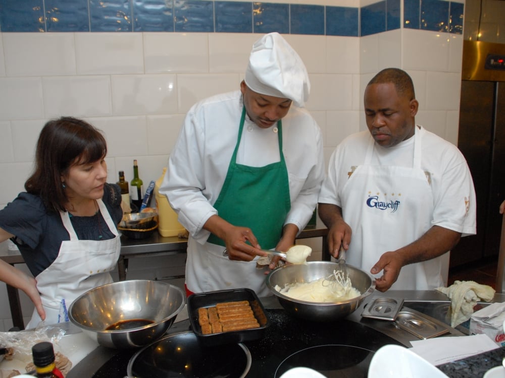 A chef prepares a Bahamian dessert while culinary students look on.