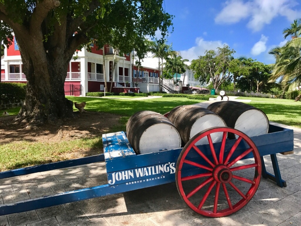 A wagon with rum barrels sits in front of a historic Bahamian building. 
