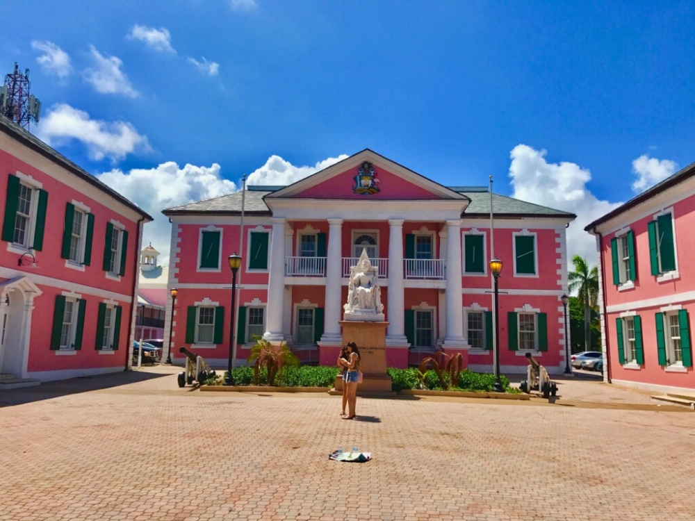 Two girls look at a map in the square in front of Government House, a vibrant pink historical building in Nassau.