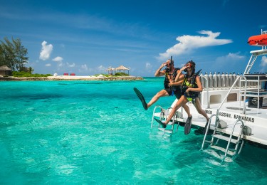 A couple in snorkeling gear jumps into the water at Sandals Royal Bahamian's Offshore Island.