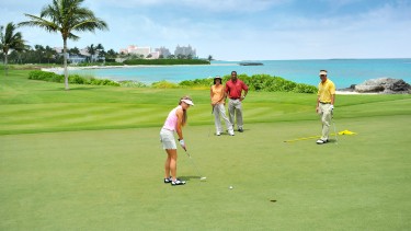 A group of people golfing with a stunning view of the ocean in the distance.