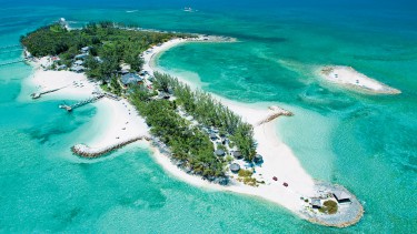 An aerial view of a white sand island filled with lush green trees and surrounded by tropical turquoise waters.