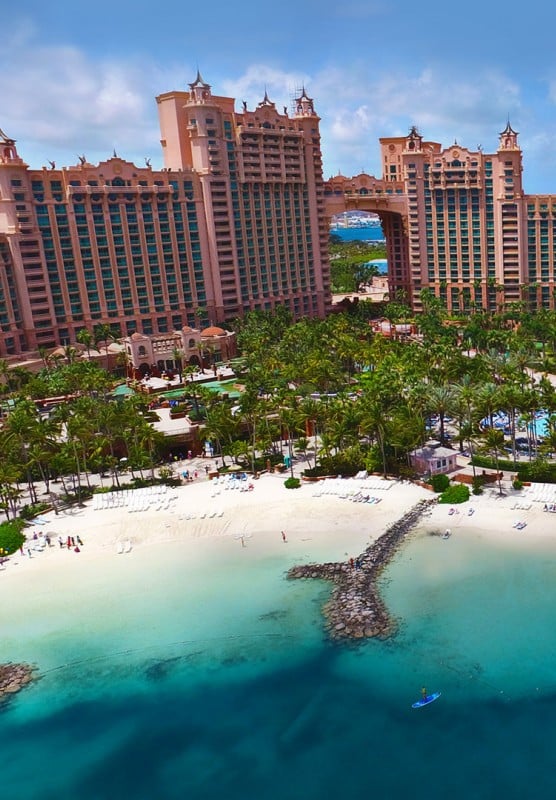 An aerial view of large resort buildings placed among lush green trees, surrounded by white sand beaches.