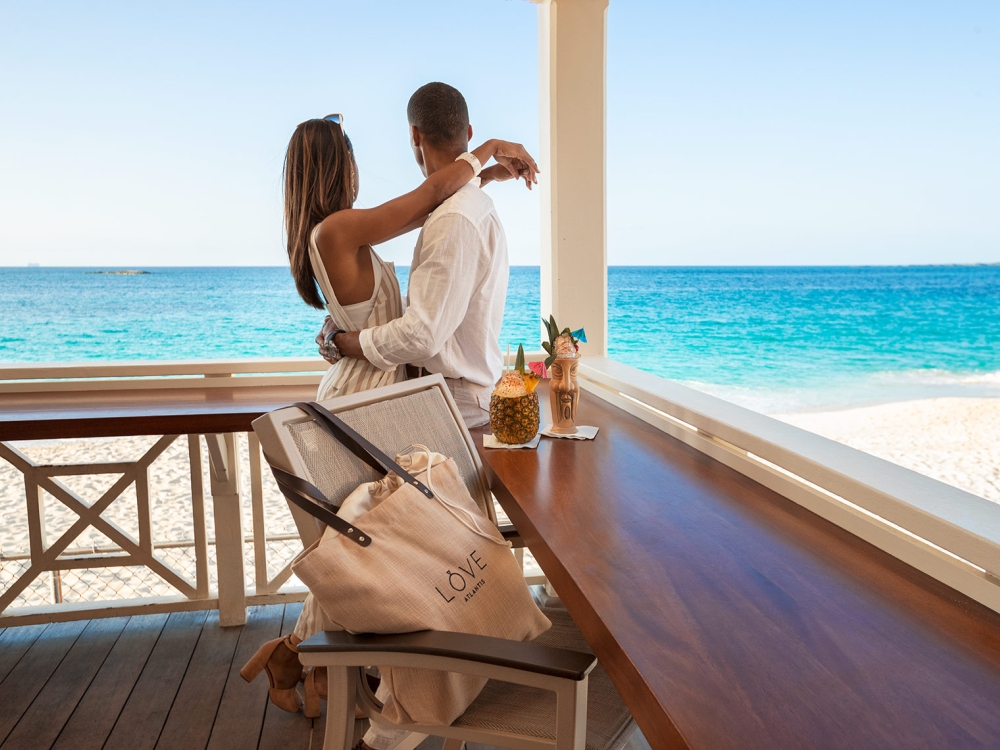 A couple embraces on a deck overlooking the bright blue Caribbean sea. 