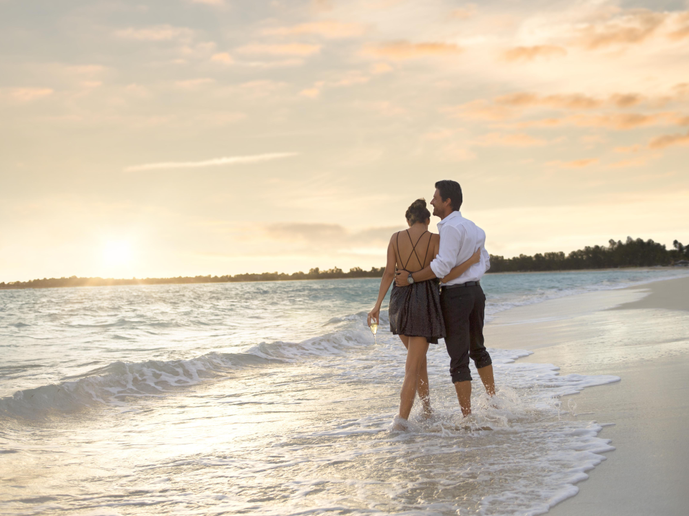 A couple walks along the water's edge on a Bahamas beach at sunset. 