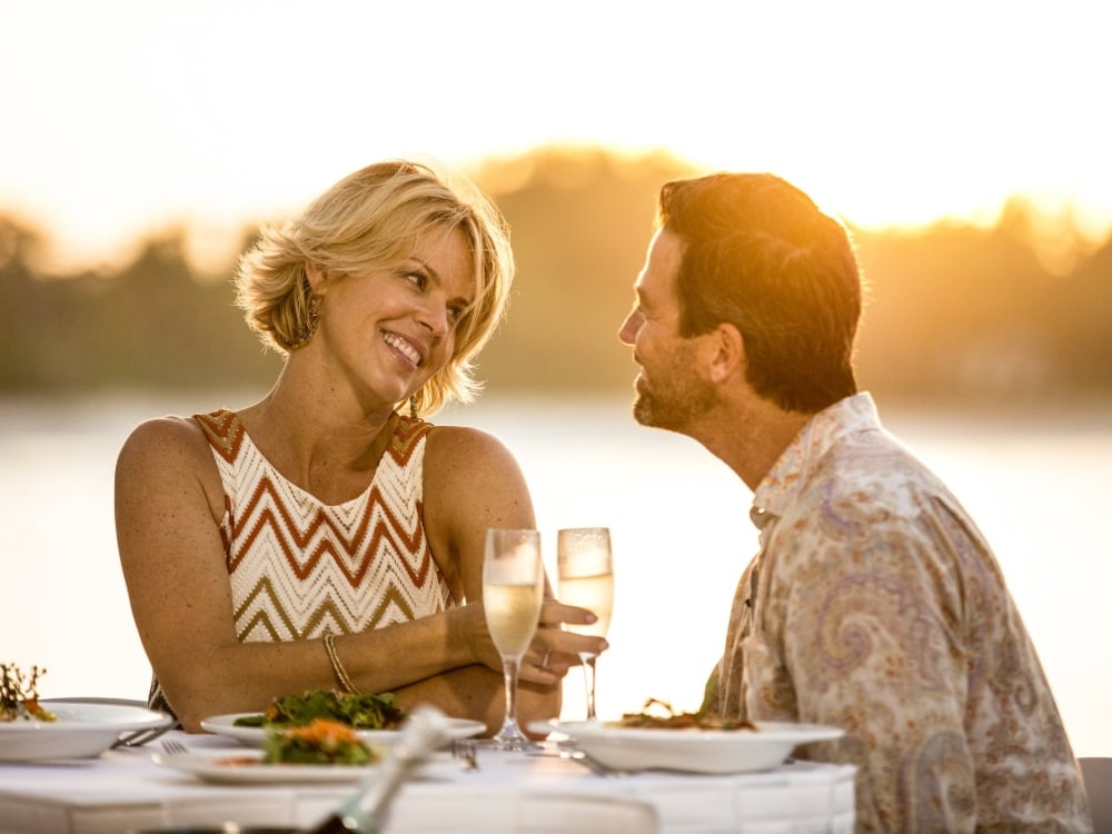 A couple toasts at a patio table at sunset.