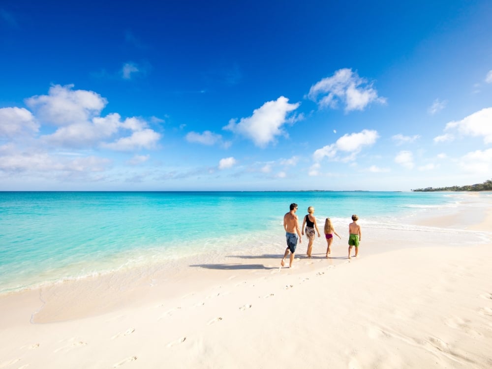 A family of four walks together along a Bahamas beach. 