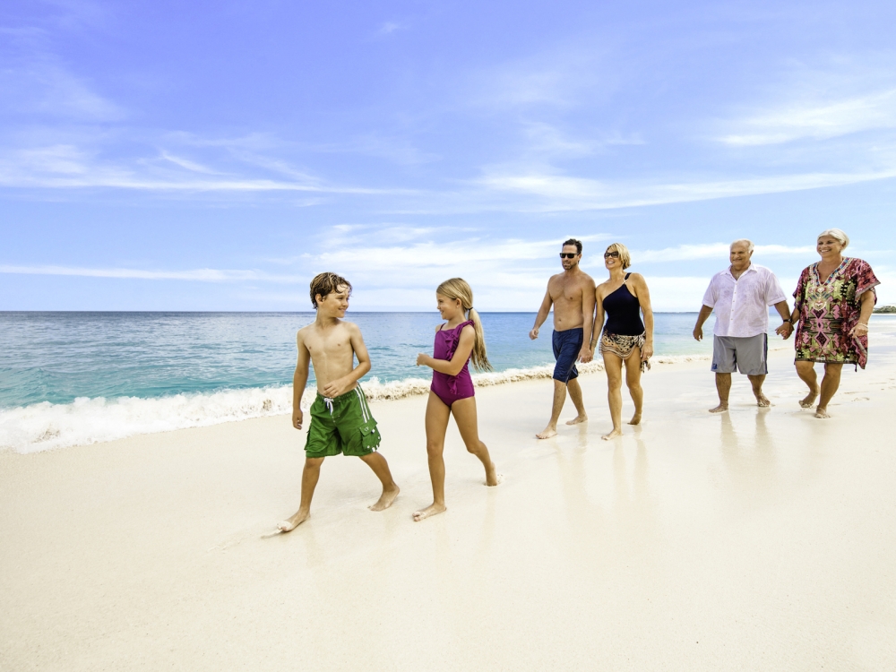 Two children, their parents, and grandparents walk on a Bahamas beach.