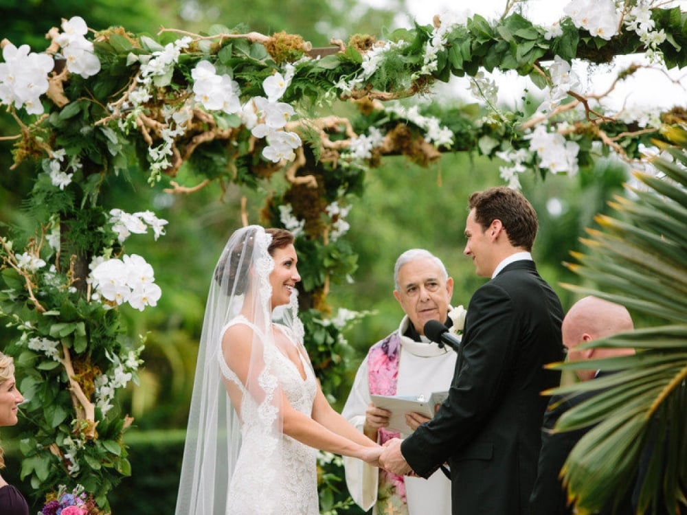 A bride and groom say their vows under lush tropical vegetation in Nassau Paradise Island