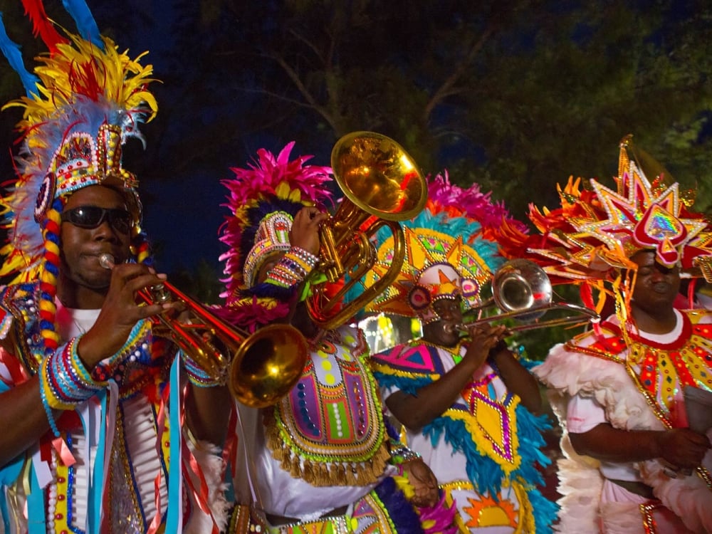 Junkanoo musicians play horns in brightly colored costumes. 