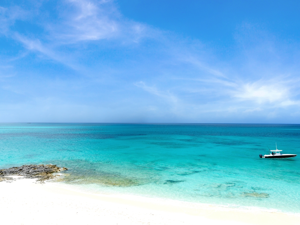 Bright blue sky, clear turquoise waters, and a small boat anchored off the shore of a Bahamas beach. 