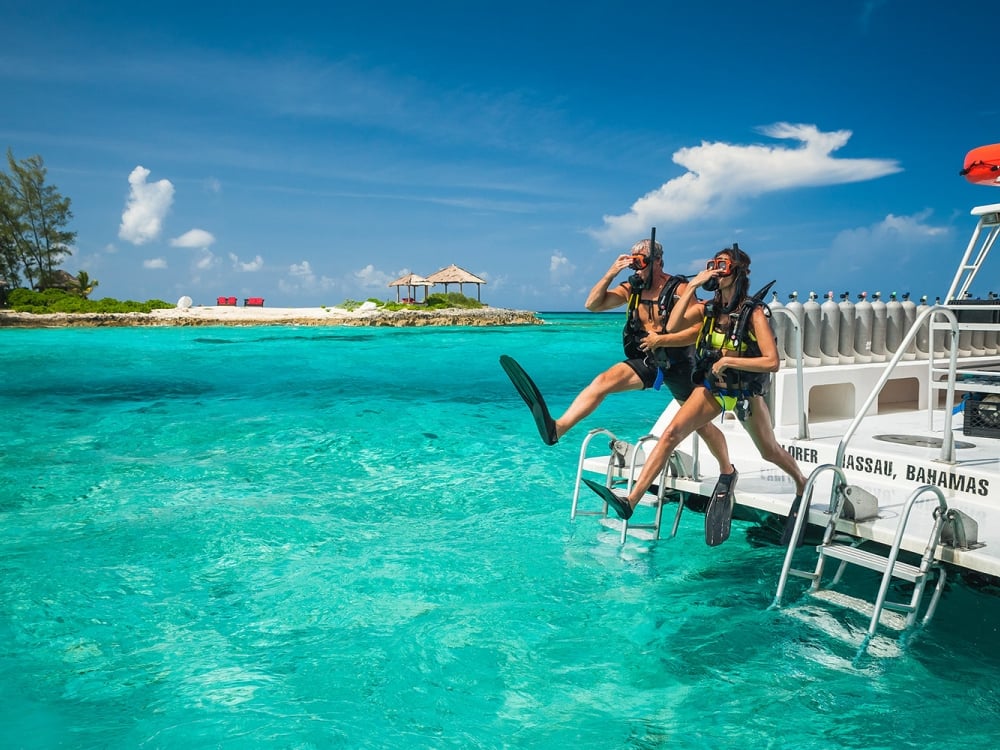 A couple in snorkeling gear jumps into the water at Sandals Royal Bahamian's Offshore Island.