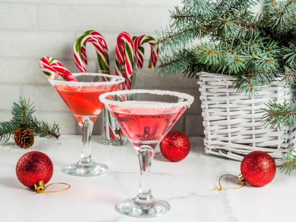 Two martini glasses filled with red liquid with candy canes in the glass and red Christmas balls on a marble countertop
