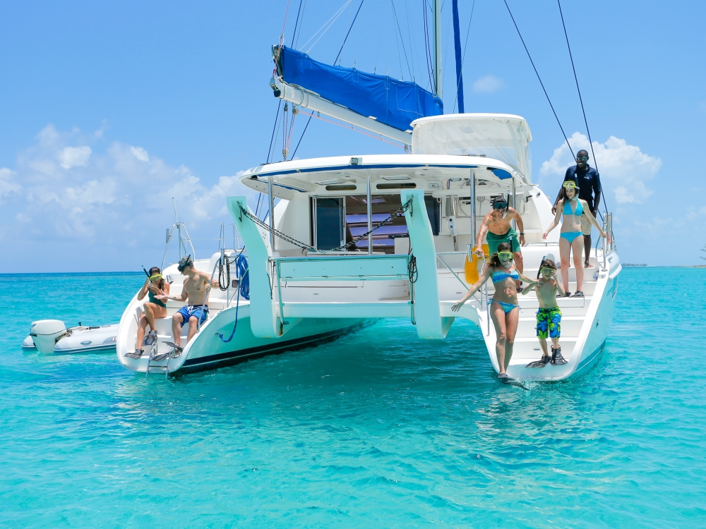 A couple and family prepare to jump off the back of a catamaran into turquoise Bahamas waters.