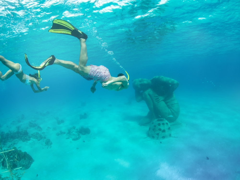 Two scuba divers swimming below the ocean surface towards a statue.