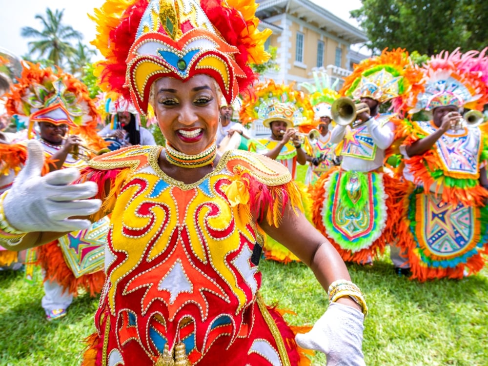 Junkanoo dancer welcoming wave with more dancers behind in orange and red colorful outfits