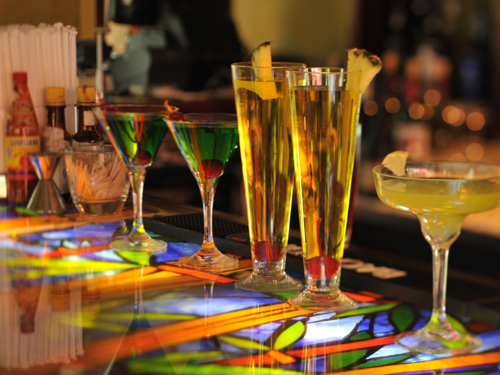 A row of tropical cocktails sits on a colorful bar.
