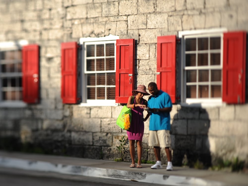 A couple look at a map outside a historic Bahamas building with red shutters.