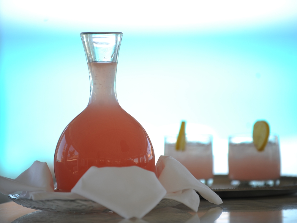 A pitcher and glasses of fruity Bahamas Breeze sits on a table by the sea.