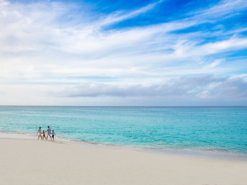 A family of four walks hand-in-hand along a Bahamas beach.