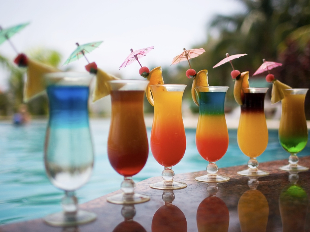 A row of colorful tropical drinks by a pool