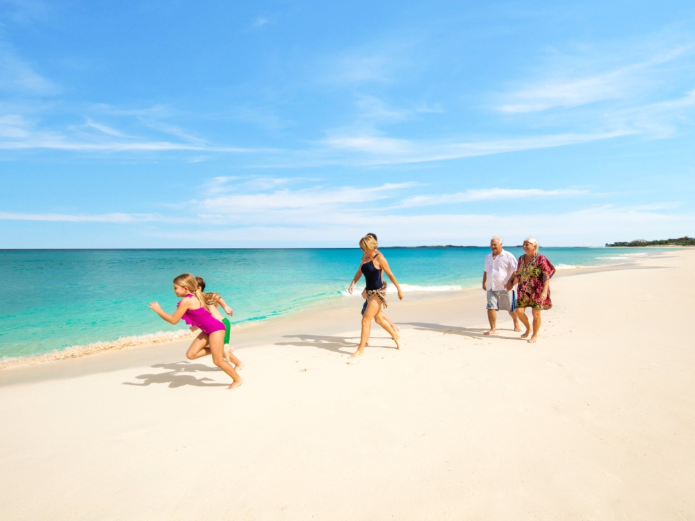 Two children run on a Bahamas beach followed by their parents and grandparents.
