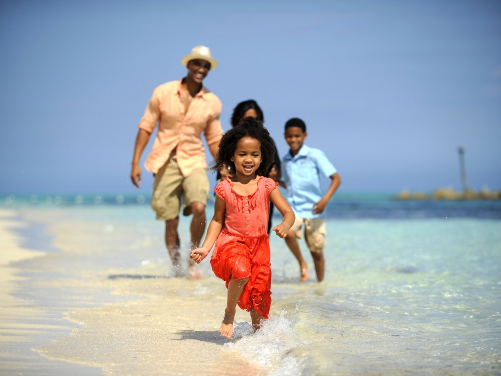 Little girl running in the water with family running behind her