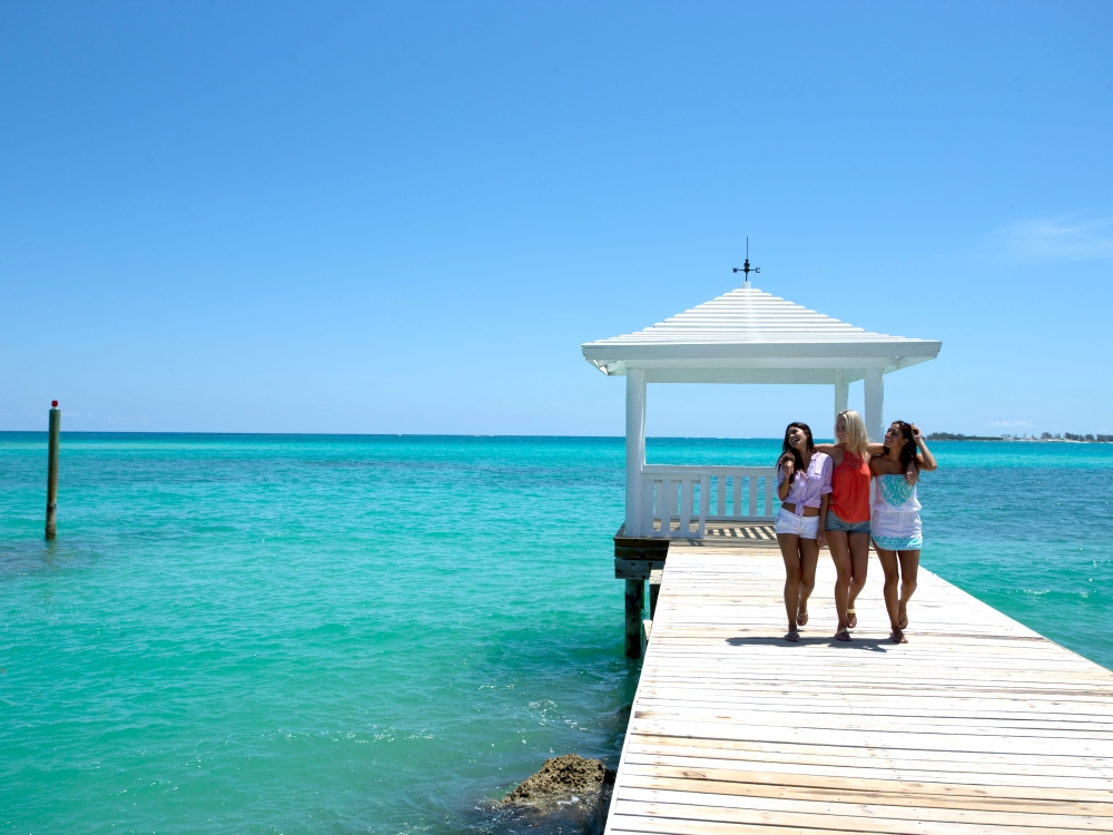 Three women walk arm-in-arm along a boardwalk in The Bahamas.