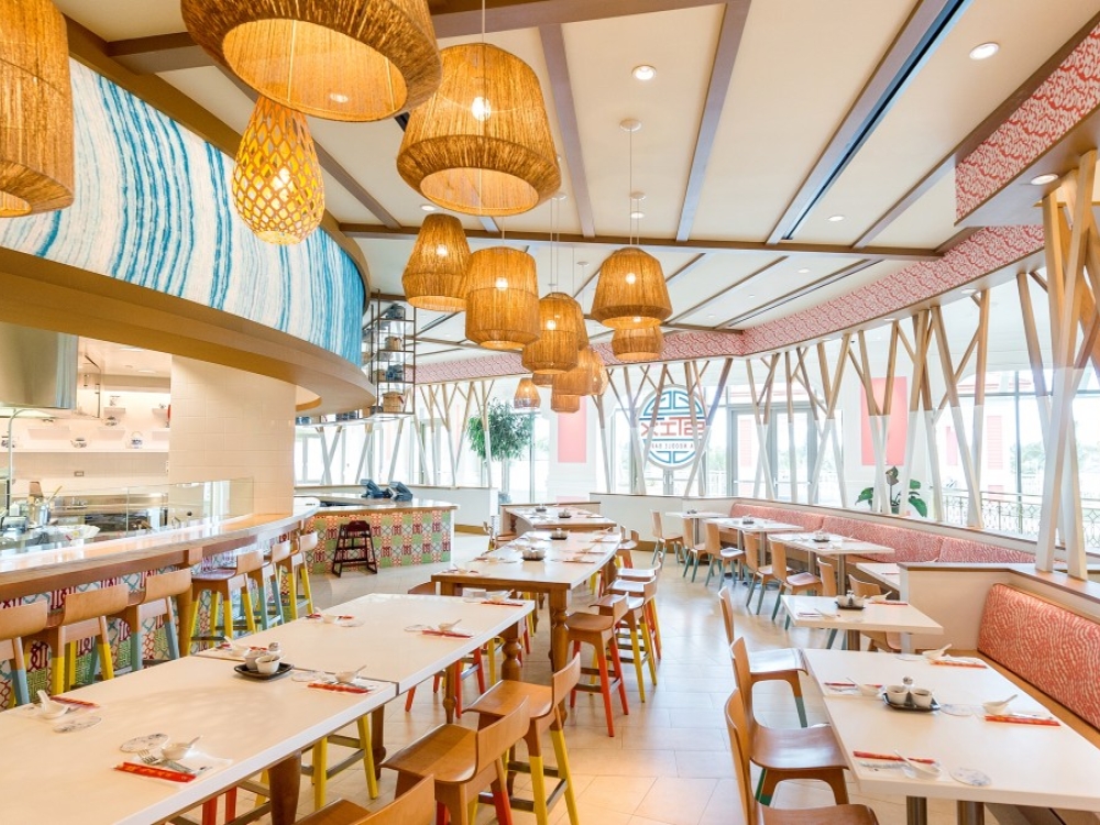 The interior of a restaurant with long wooden tables and decorative hanging light fixtures.