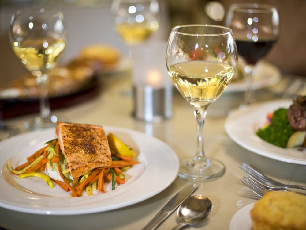 A photograph of a dining table filled with wine glasses and dishes of food.