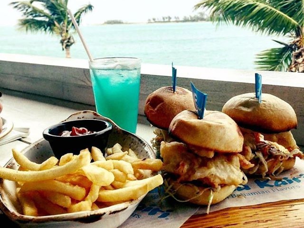 French fries, burgers and a blue icy beverage sit atop a beach-side table.