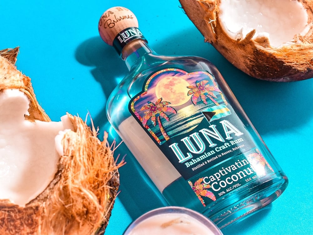 luna rum bottle lays on blue background with broken open coconut