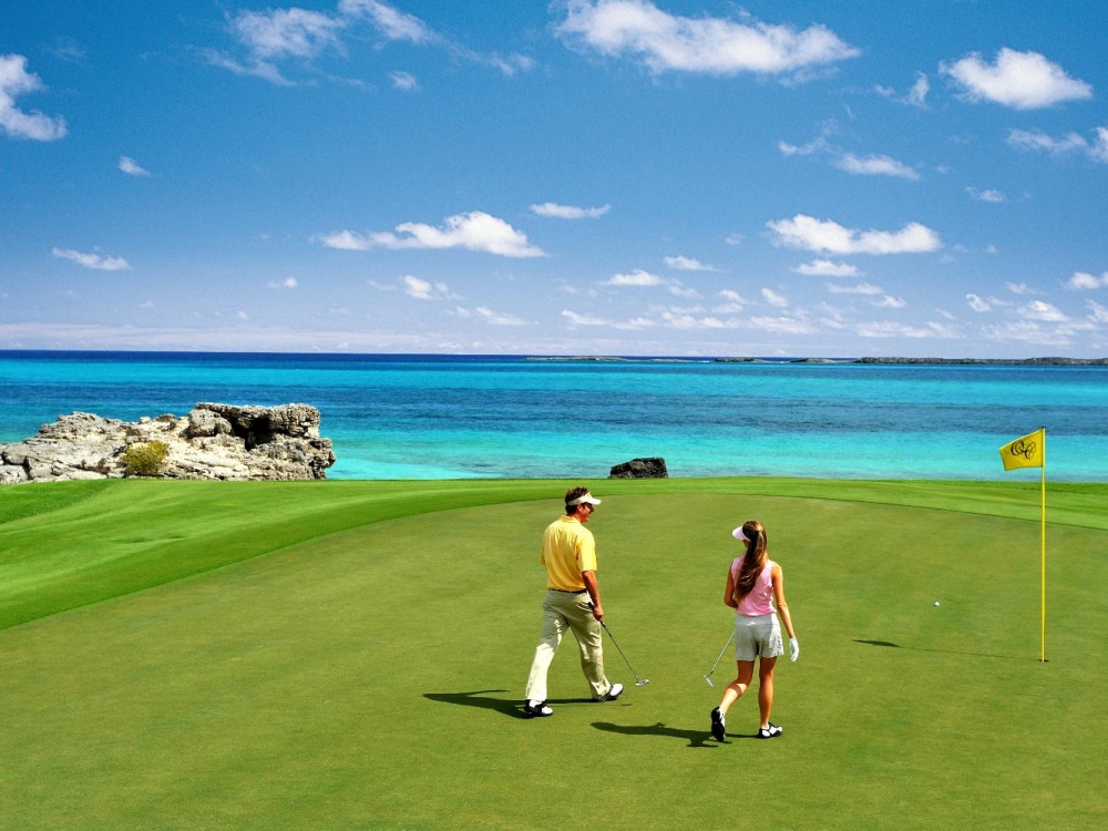 A man and a woman walk towards a hole on a golf course in The Bahamas.