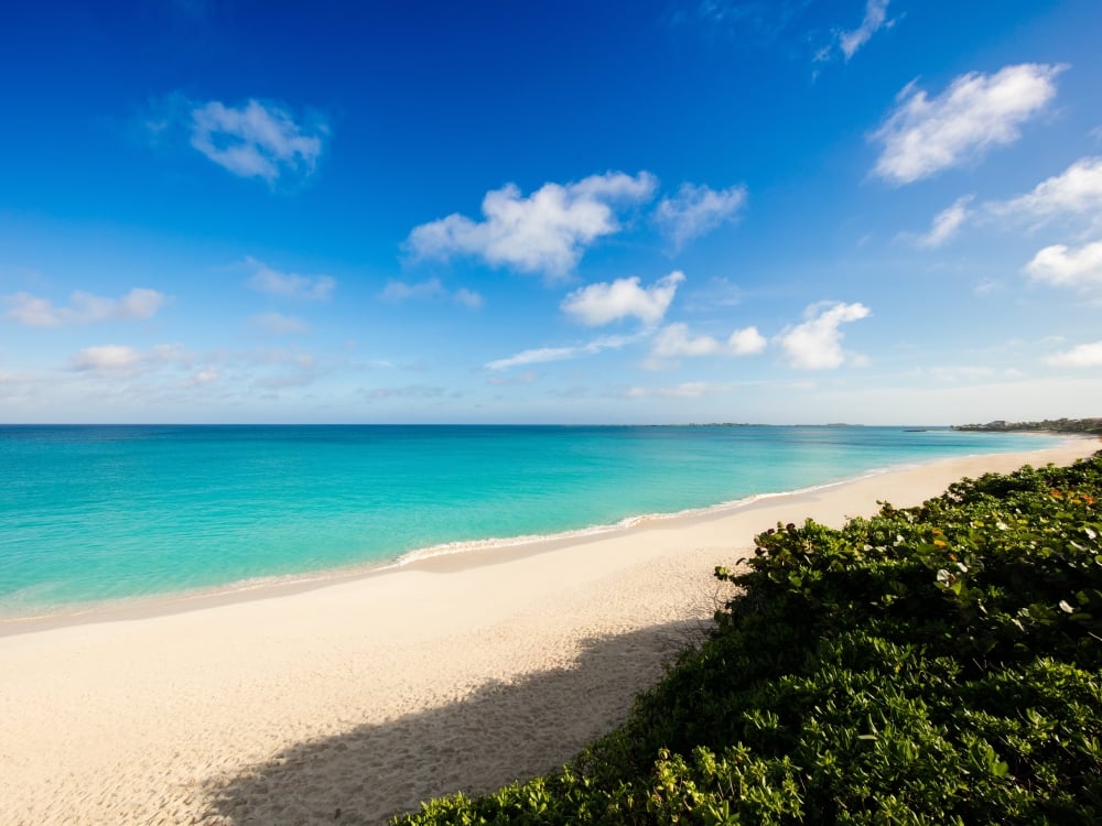 An empty tropical beach with white sand and bright turquoise water.