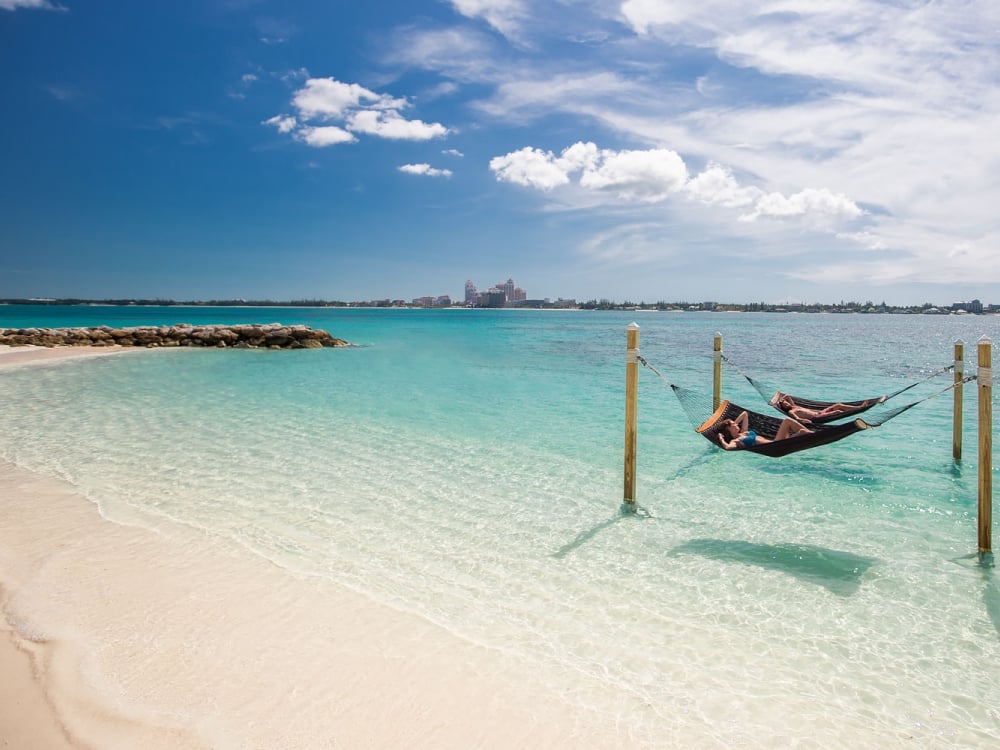 Beach scene with a couple laying in two hammocks above water