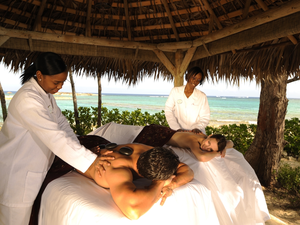 A couple looks at each other while receiving a couples massage on a beach in The Bahamas. 
