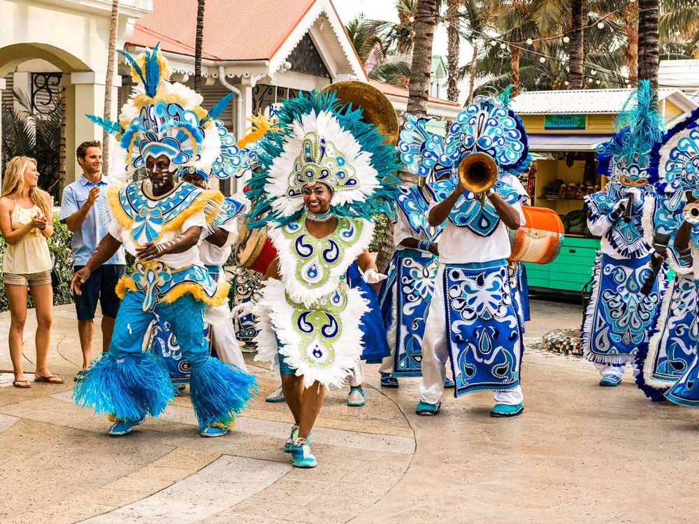People dressed in intricate costumes walk down a sunny street.