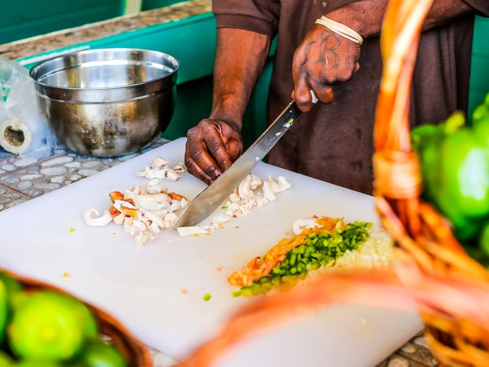 A man slices vegetables on a white cutting board.