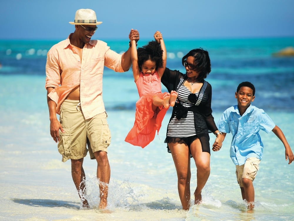 A family of four walking through tropical beach waters.