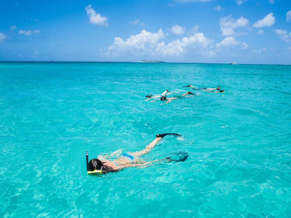 A family of four snorkels in clear turquoise waters.
