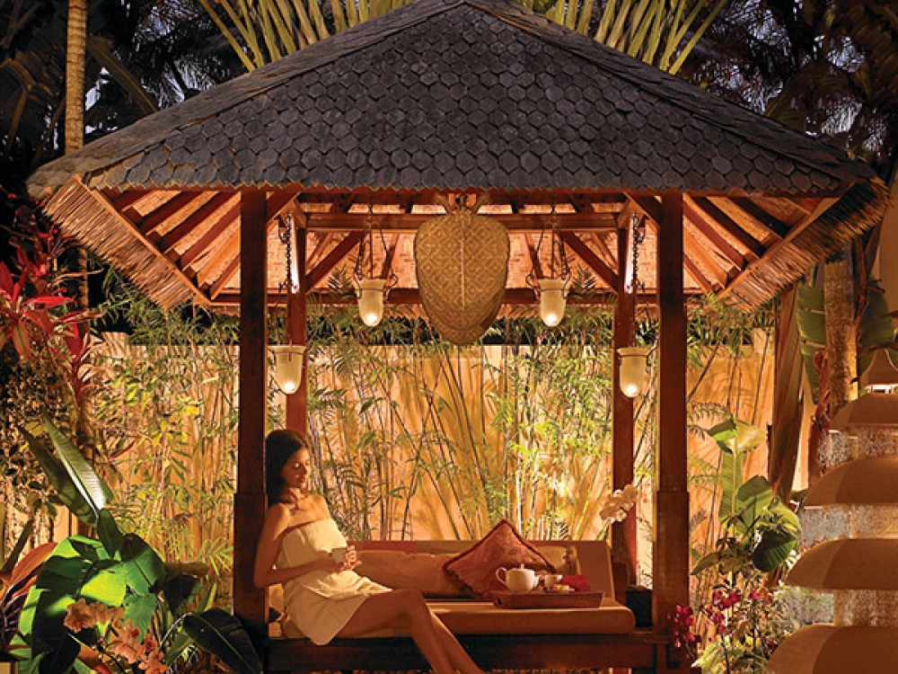 A woman relaxes in an opulent gazebo at twilight.