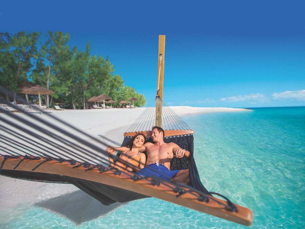 A couple relaxes on a hammock on a beach at Sandals Royal Bahamian.