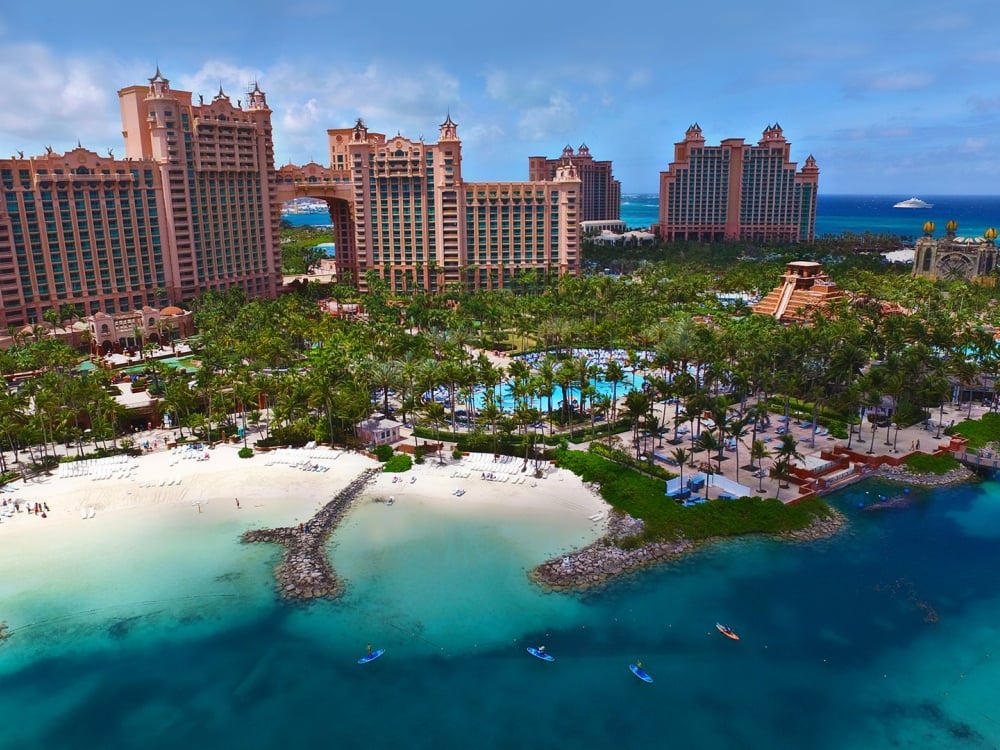 An aerial view of large resort buildings placed among lush green trees, surrounded by white sand beaches.