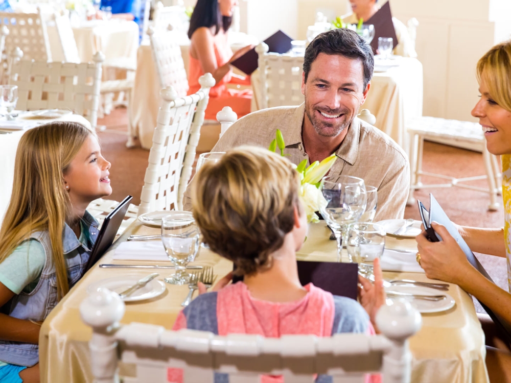 A family of four have dinner in a sunny outdoor restaurant.