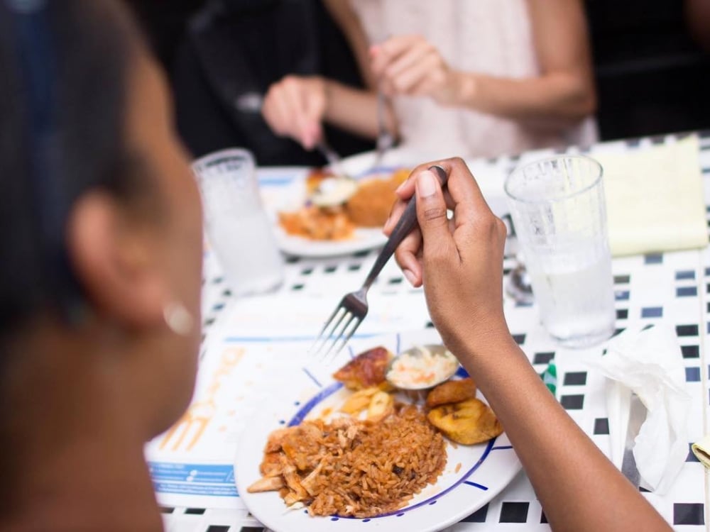 A woman lifts a fork to sample a plate of Bahamian food. 