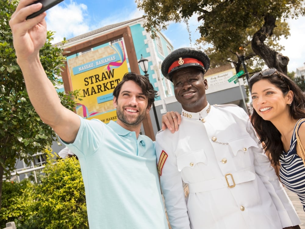A young couple takes a selfie with a Bahamian policeman outside the Nassau Straw Market.