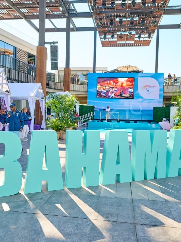 Two dancers pose in front of a sign that says Bahamas.