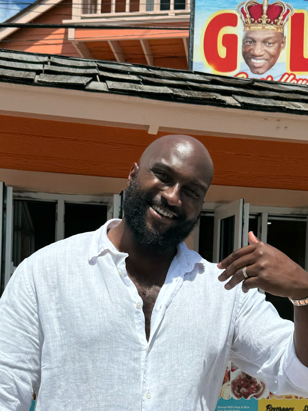 A man stands in front of a restaurant in the middle of the frame.